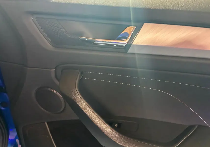 Détail de la porte côté gauche du Skoda Kodiaq 2023 bleu, avec garniture noire, surpiqûres blanches et insert bois clair.