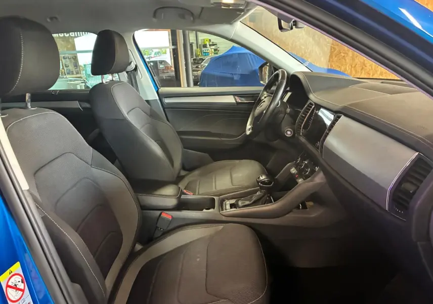 Intérieur du Skoda Kodiaq 2023 bleu, vue côté gauche montrant les sièges tissu noirs et le tableau de bord moderne.
