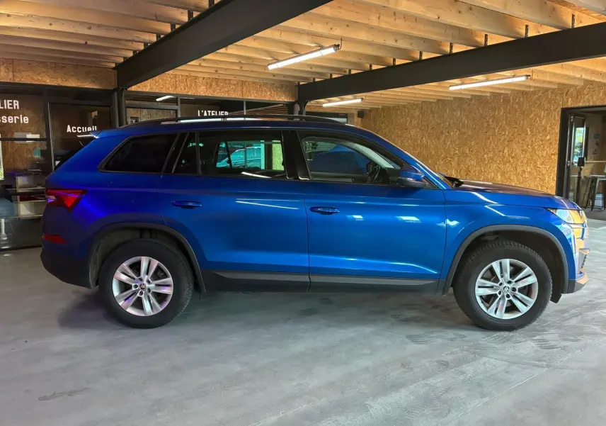 Vue de profil côté gauche d'un Skoda Kodiaq bleu 2023 garé en intérieur, soulignant ses lignes SUV et ses jantes alliage.