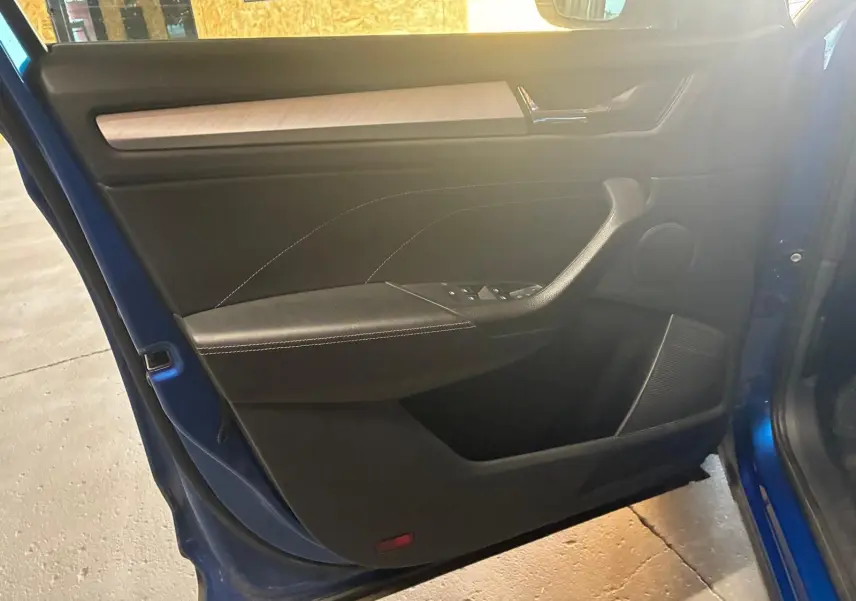 Vue intérieure de la porte avant gauche d’un Skoda Kodiaq bleu 2023, avec garniture noire et insert bois clair.