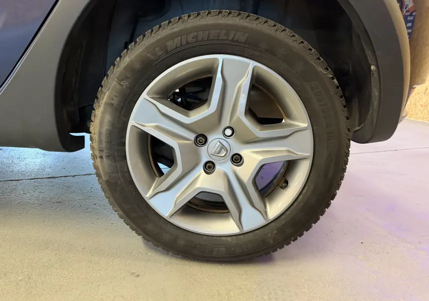 Gros plan sur la roue avant droite d'une Dacia Sandero Stepway bleu, jante alliage à cinq branches et pneu Michelin hiver.