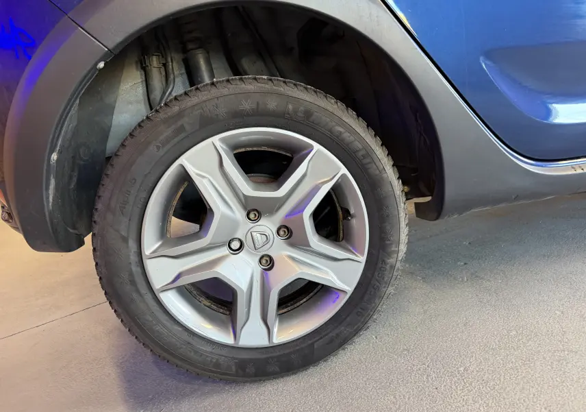 Gros plan sur la roue avant gauche d'une Dacia Sandero Stepway bleue, mettant en valeur la jante alliage et le pneu Michelin.