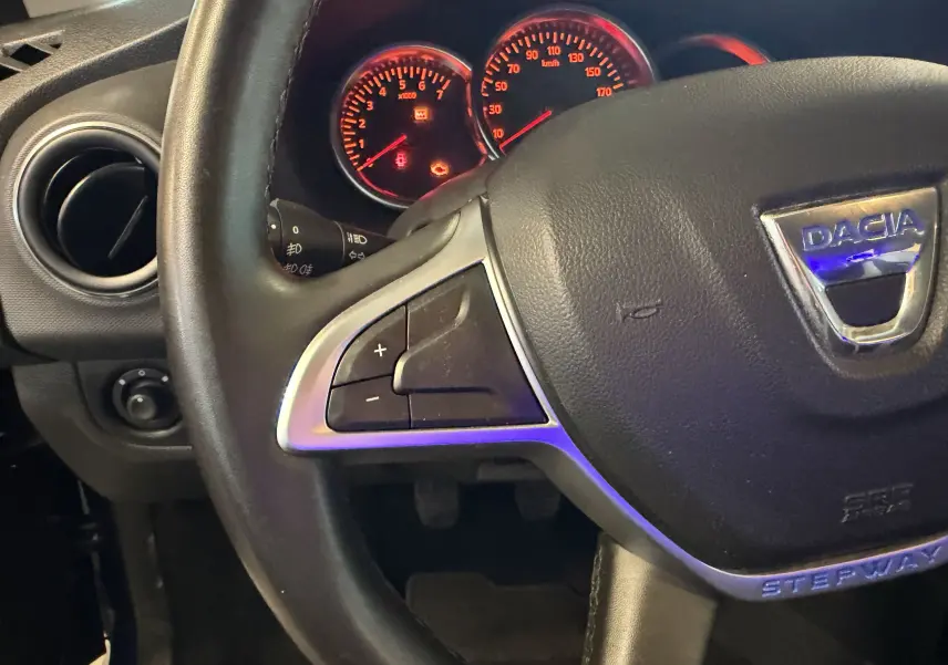 Gros plan sur le volant noir avec logo Dacia et tableau de bord éclairé du Dacia Sandero Stepway bleu de 2019.