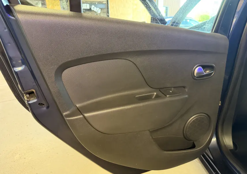 Vue intérieure de la porte arrière gauche bleu foncé de la Dacia Sandero Stepway 2019 avec panneau noir et haut-parleur intégré.