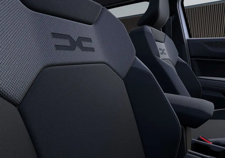 Gros plan sur les sièges avant en tissu gris foncé avec logo Dacia embossé, intérieur moderne et épuré.