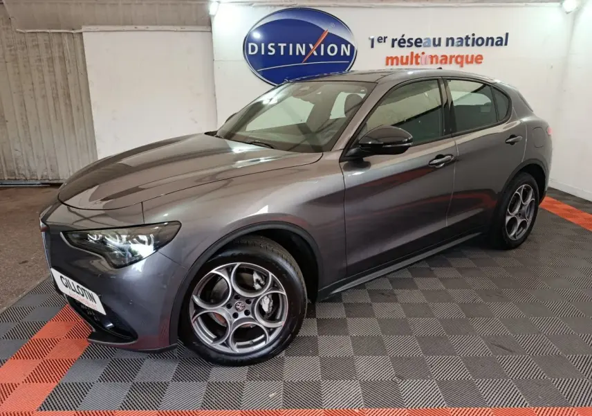 Alfa Romeo Stelvio gris foncé en 3/4 avant droit, avec phares LED et jantes distinctives à cinq cercles.