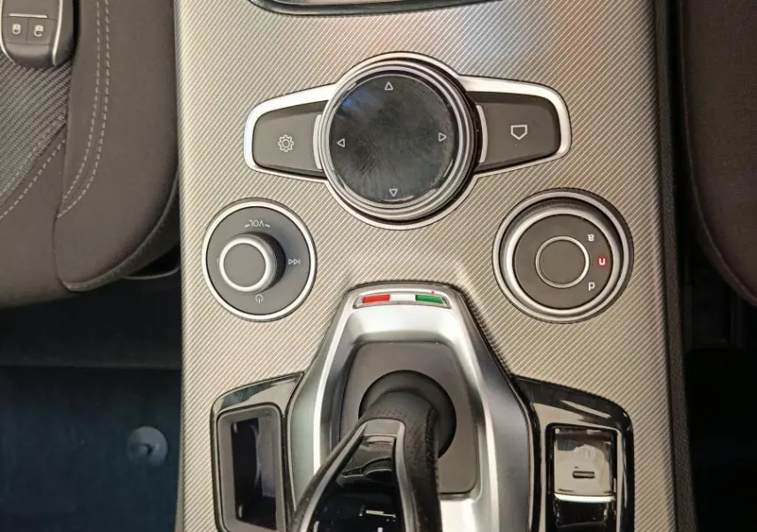 Vue plongeante sur la console centrale gris foncé de l'Alfa Romeo Stelvio 2024 avec levier de vitesses automatique et molette de contrôle.