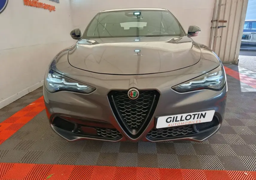 Vue frontale d'un Alfa Romeo Stelvio gris foncé 2024 avec calandre en V et phares LED allumés.