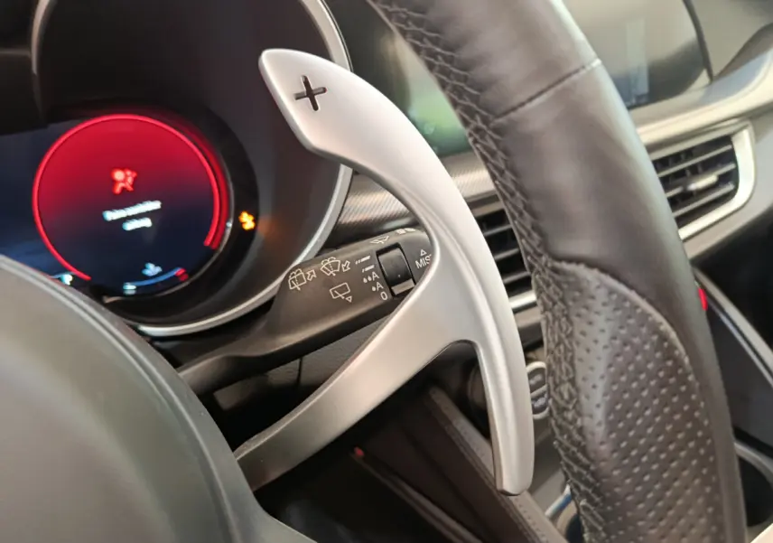 Gros plan sur la palette de changement de vitesse alu côté droit du volant cuir perforé d’un Alfa Romeo Stelvio gris foncé.
