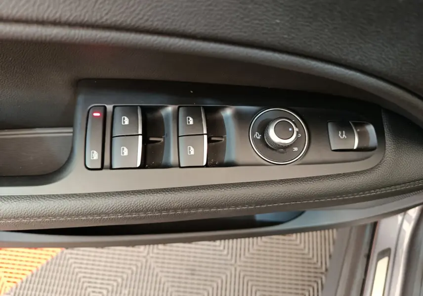 Vue rapprochée des commandes de lève-vitres et rétroviseurs sur la porte côté gauche d'un Alfa Romeo Stelvio gris foncé.