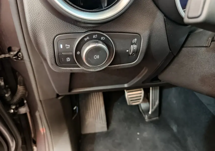 Gros plan sur les commandes d’éclairage et les pédales côté conducteur de l’Alfa Romeo Stelvio gris foncé 2024.