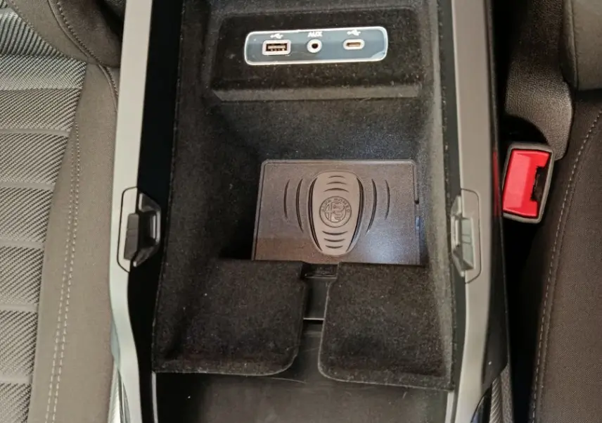 Vue plongeante sur la console centrale noire de l'Alfa Romeo Stelvio 2024 avec ports USB, prise AUX et zone de recharge sans fil.