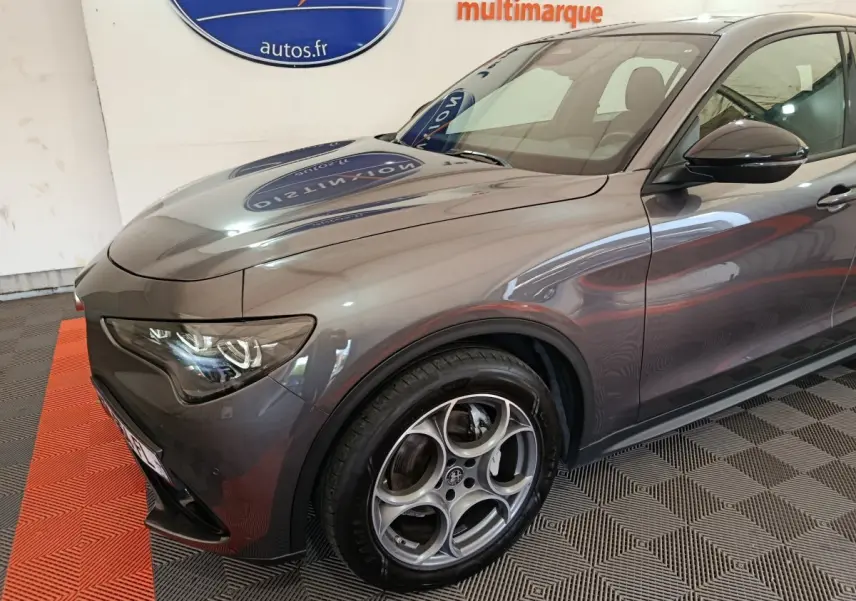 Vue 3/4 avant droit de l'Alfa Romeo Stelvio gris foncé avec jantes distinctives et phares LED ellipsoïdaux.