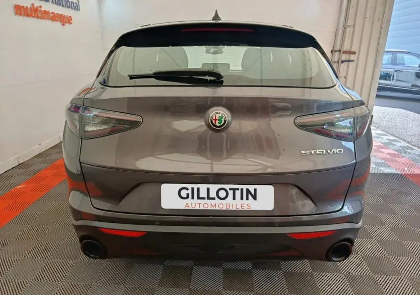 Vue arrière d'un Alfa Romeo Stelvio gris foncé avec feux effilés et double sortie d'échappement ronde.