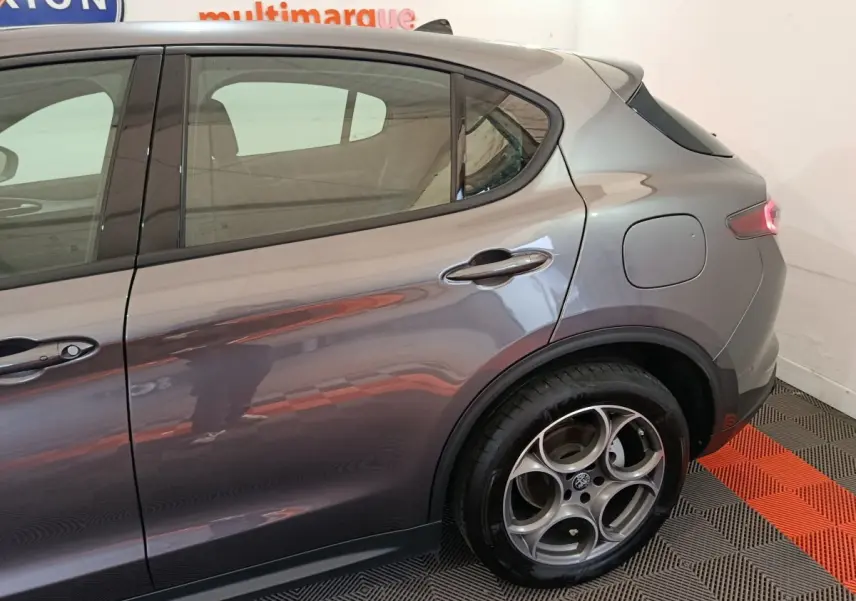 Vue latérale arrière droite d’un Alfa Romeo Stelvio gris foncé, mettant en valeur la jante spécifique et la trappe à carburant.