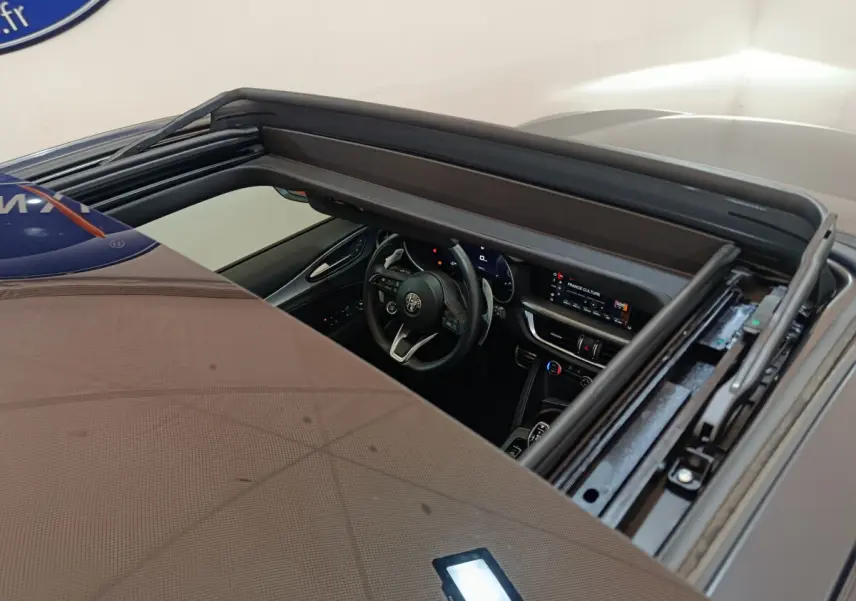 Vue plongeante sur l'intérieur du tableau de bord et volant d'un Alfa Romeo Stelvio gris foncé avec toit ouvrant ouvert.
