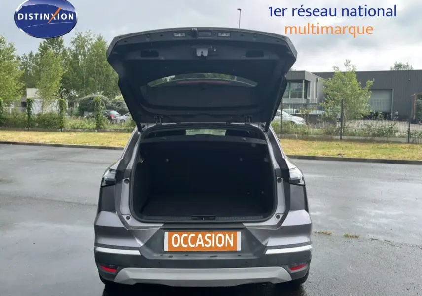 Vue arrière d'une Renault Symbioz gris cassiopée métal avec coffre ouvert sur un parking extérieur.