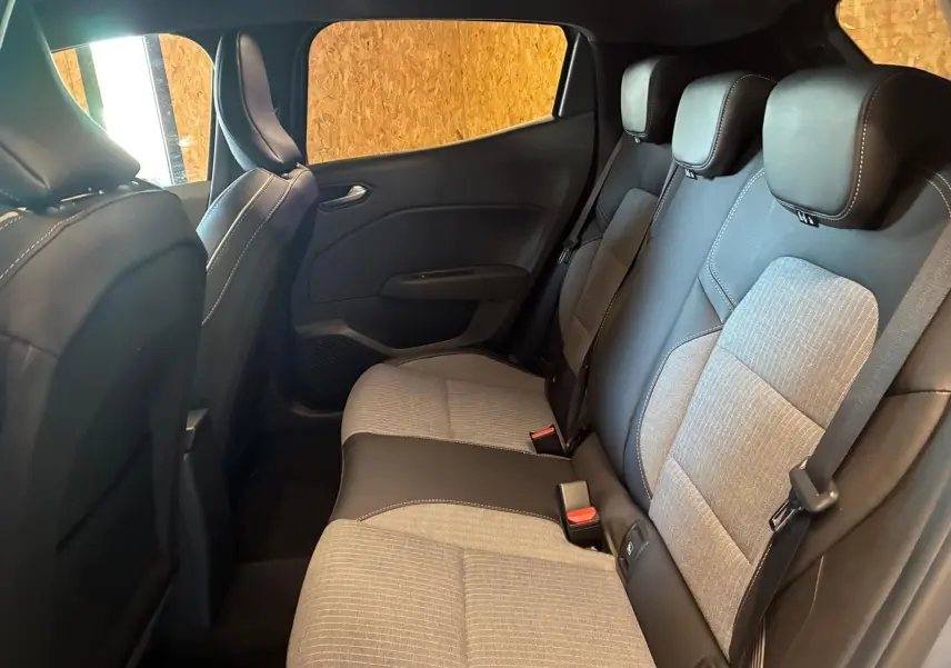 Vue intérieure arrière de la Renault Clio 2025, sièges tissu gris clair avec surpiqûres et garnitures noires.