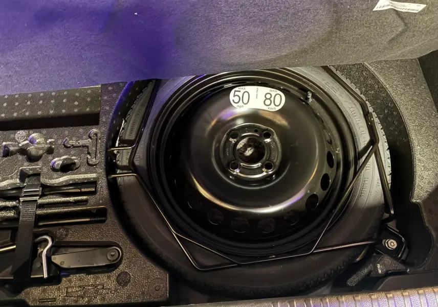 Vue rapprochée de la roue de secours noire et des outils de bord dans le coffre d'une Renault Clio gris schiste 2025.