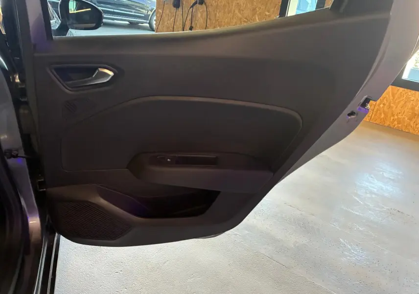 Détail de la porte arrière gauche ouverte d’une Renault Clio gris schiste, intérieur noir avec commande de vitre.