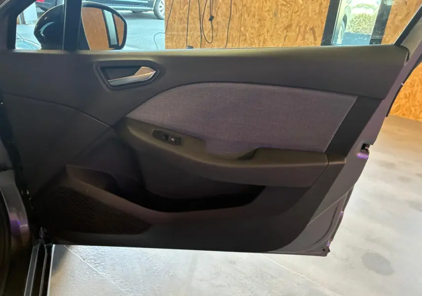 Vue intérieure de la porte avant gauche de la Renault Clio gris schiste, avec habillage tissu gris et commande de vitre.