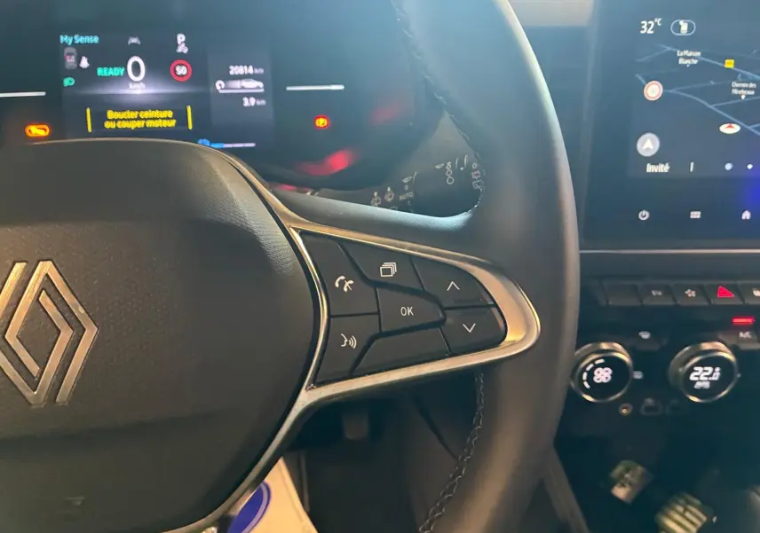 Gros plan sur le volant noir de la Renault Clio 2025 avec commandes intégrées et tableau de bord numérique lumineux.