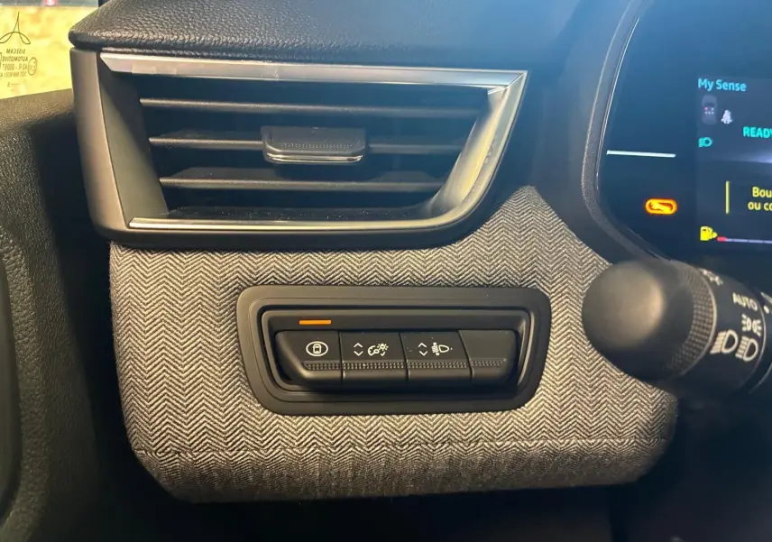 Détail intérieur côté gauche de la planche de bord de la Renault Clio 2025, tissu gris à chevrons avec commandes d’éclairage.