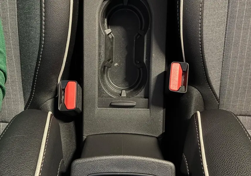 Vue plongeante sur la console centrale de la Renault Clio hybride 2025, avec porte-gobelets et boutons de frein à main électronique.