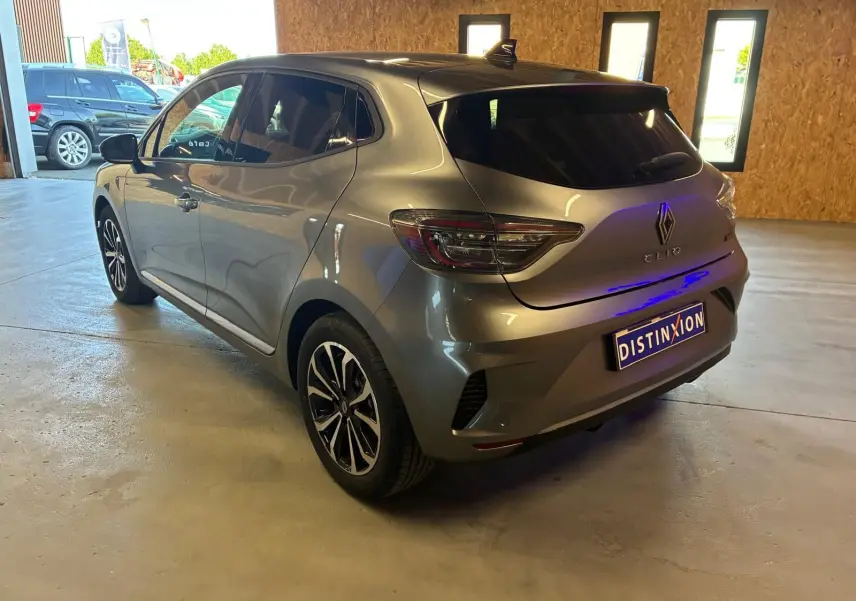 Vue 3/4 arrière droite d'une Renault Clio gris schiste, avec feux LED et jantes alliage noires, en intérieur lumineux.