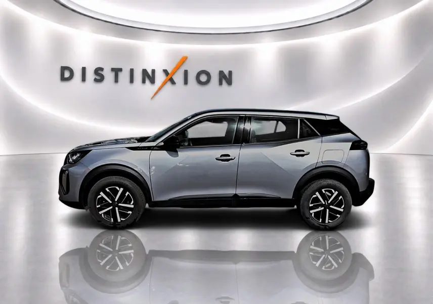 Profil côté gauche d’un Peugeot 2008 gris 2025 avec toit noir et jantes à motif bicolore dans un showroom lumineux.