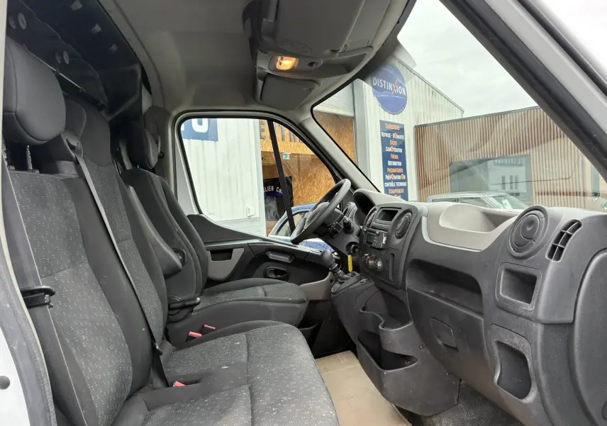 Vue intérieure côté conducteur de l'Opel Movano Fourgon blanc 2017, montrant les sièges tissu gris et le tableau de bord noir.