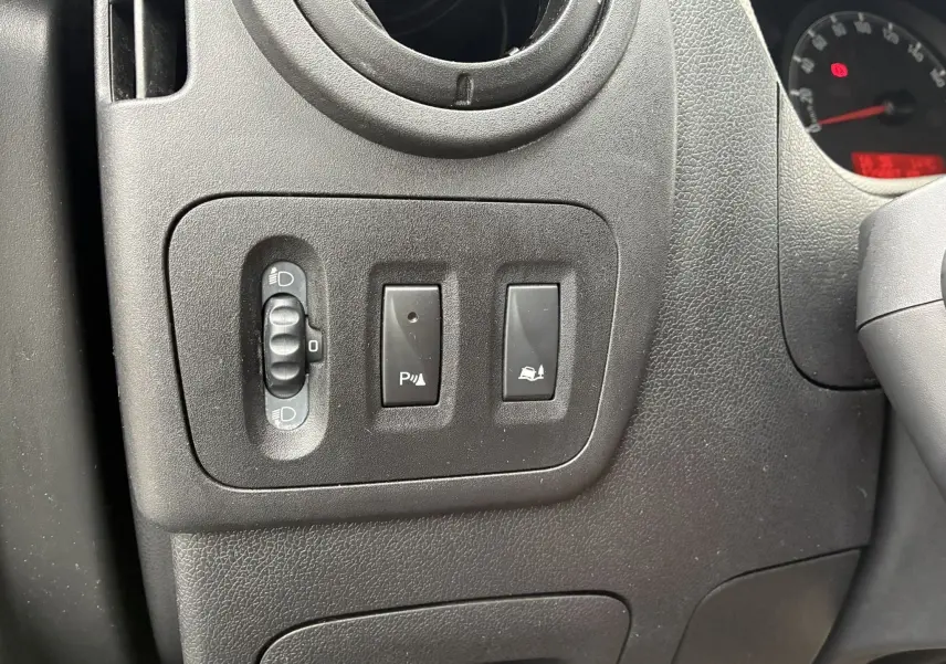 Gros plan sur les commandes de réglage des phares et d'assistance au stationnement du tableau de bord noir d'un Opel Movano Fourgon blanc.