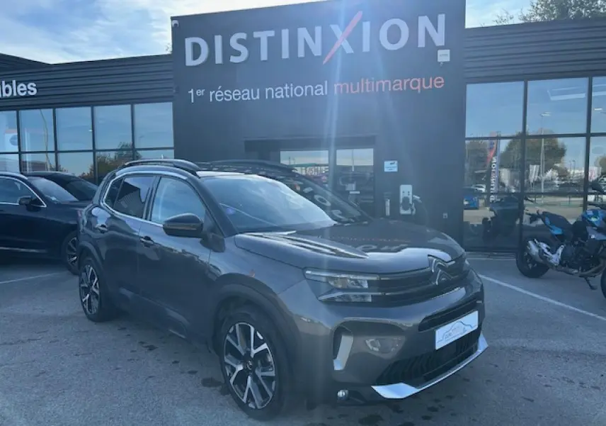 Citroën C5 Aircross gris platinium en 3/4 avant droit, avec barres de toit et jantes alliage visibles.
