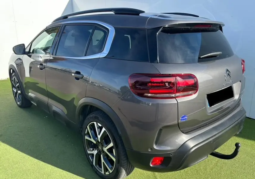 Vue 3/4 arrière droit du Citroën C5 Aircross gris platinium avec barres de toit et attelage visible.