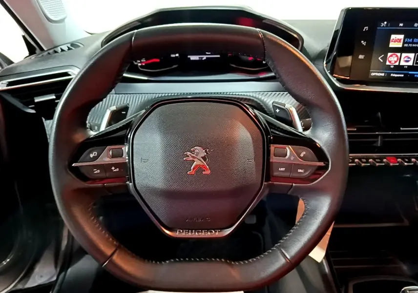 Vue rapprochée du volant cuir multifonctions noir du Peugeot 2008 2021 avec tableau de bord et écran tactile visibles.