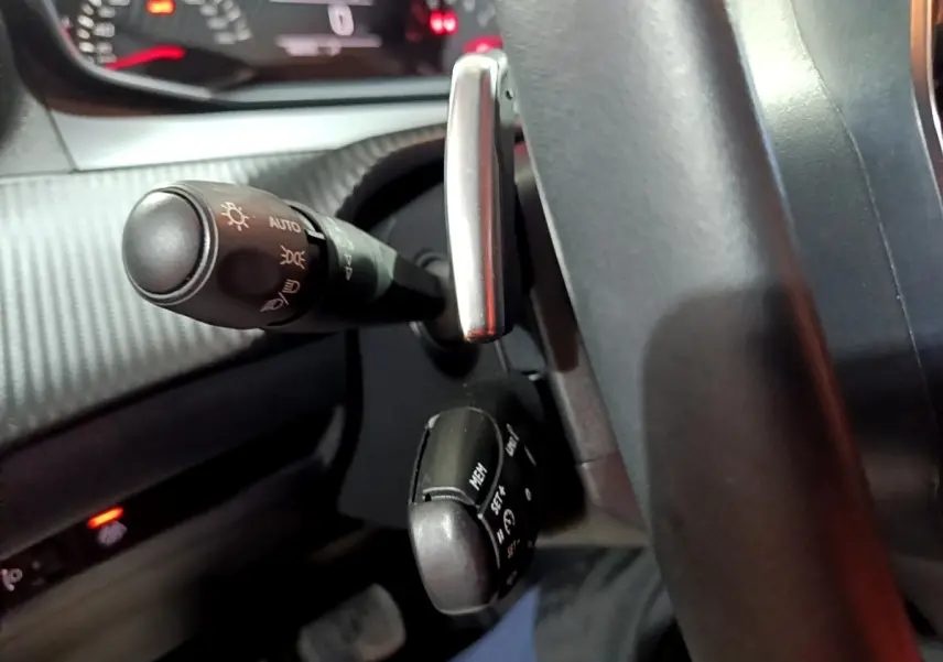 Gros plan sur le volant cuir et les commandes au volant du Peugeot 2008 gris clair, tableau de bord en arrière-plan.