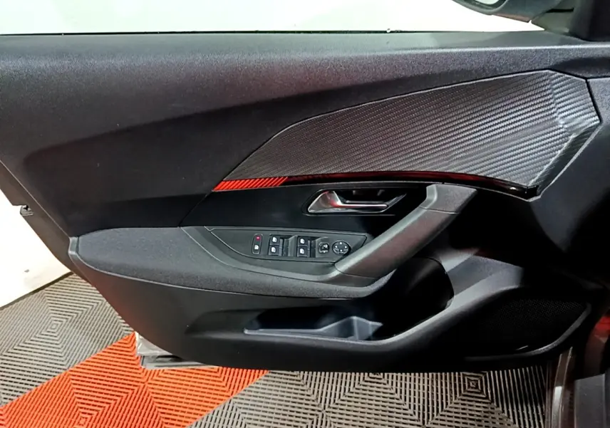 Vue intérieure côté gauche de la porte avant d’un Peugeot 2008 gris clair, avec commandes électriques et insert décoratif noir.