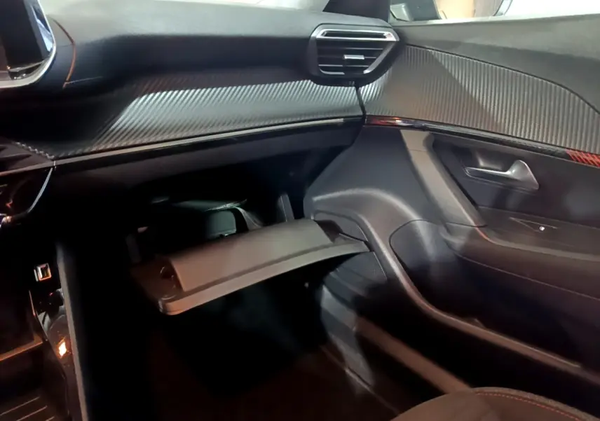 Intérieur côté passager du Peugeot 2008 gris clair, vue sur la boîte à gants ouverte et le tableau de bord noir avec inserts carbone.