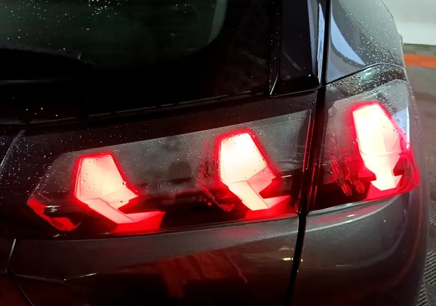 Gros plan sur les feux arrière allumés d'une Peugeot 2008 gris clair, vue côté droit sous la pluie.