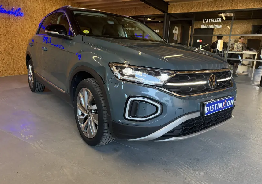Volkswagen T-Roc bleu 3/4 avant droit, avec calandre distinctive et jantes alliage, en intérieur showroom.