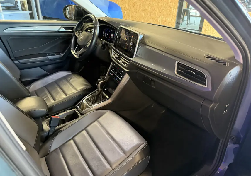 Vue intérieure côté conducteur du Volkswagen T-Roc bleu 2022, avec tableau de bord numérique et sellerie cuir noire.
