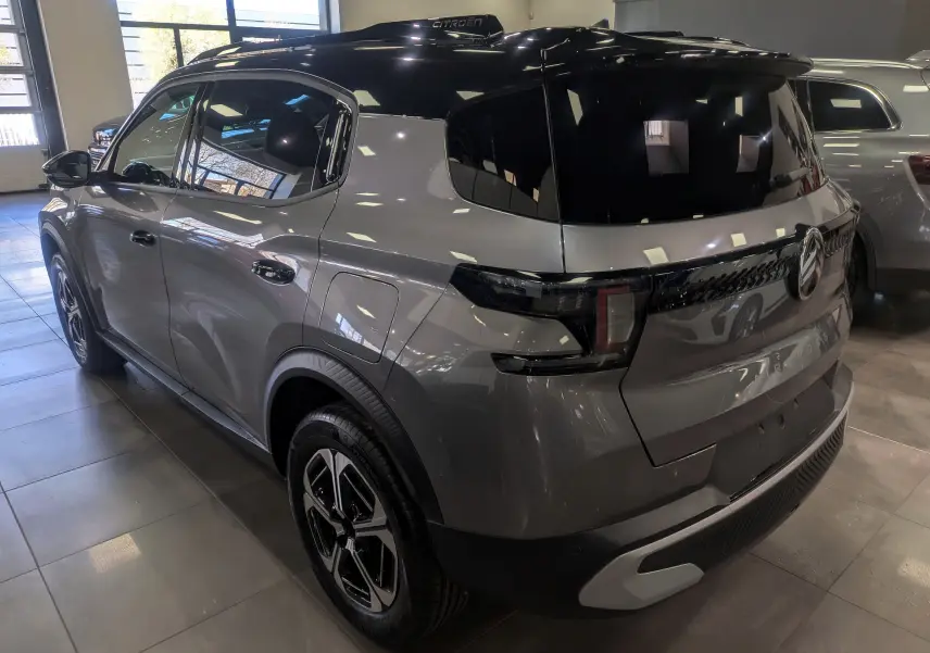 Vue 3/4 arrière droite d'une Citroën C3 Aircross hybride gris Mercury avec toit noir brillant en intérieur showroom.