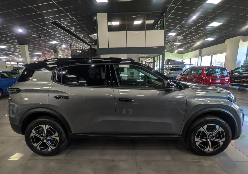 Vue de profil côté gauche d'un Citroën C3 Aircross hybride gris Mercury avec toit noir en showroom.