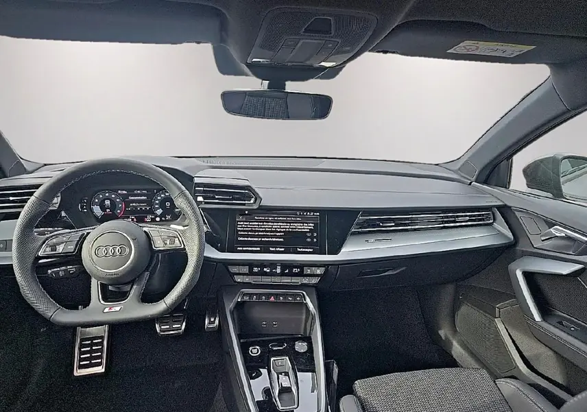 Vue avant intérieure de l'Audi A3 Sportback 2026, tableau de bord noir avec volant sport multifonction et écran central tactile.