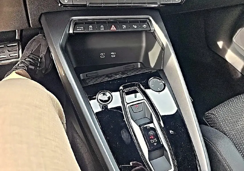 Vue plongeante sur la console centrale noire brillante de l'Audi A3 Sportback 1.5 TFSI 150 hybride, avec levier de vitesses automatique.