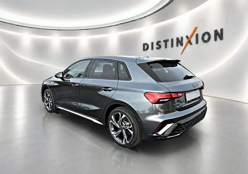 Audi A3 Sportback gris Daytona vue 3/4 arrière droit dans un showroom lumineux avec jantes alu distinctives.
