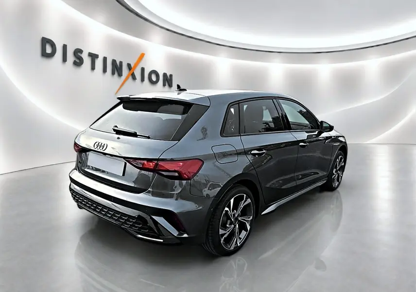 Audi A3 Sportback gris Daytona vue 3/4 arrière droit dans un showroom lumineux avec jantes alu distinctives.