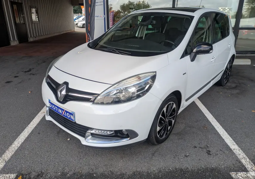 Renault Scénic IV blanc en 3/4 avant droit, avec jantes noires et chrome autour des antibrouillards.