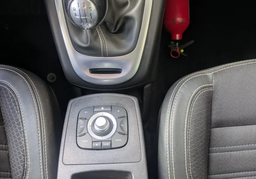 Vue plongeante sur la console centrale noire du Renault Scénic IV, avec levier de vitesse manuel et sièges en tissu gris.
