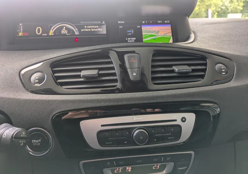 Vue rapprochée du tableau de bord noir du Renault Scenic IV blanc, avec écran digital et commandes centrales visibles.